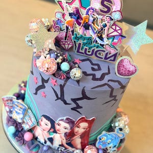May include: A decorated cake with a purple and teal color scheme. The cake features images of animated figures, disco balls, and star-shaped decorations. The top of the cake has a topper with the number 5 and the word "Luck".