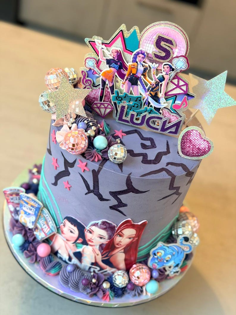 May include: A decorated cake with a purple and teal color scheme. The cake features images of animated figures, disco balls, and star-shaped decorations. The top of the cake has a topper with the number 5 and the word "Luck".
