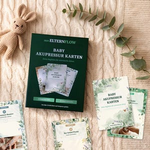 K&ouml;nnte beinhalten: Eine dunkelgr&uuml;ne Schachtel mit der Aufschrift DEIN ELTERNFLOW BABY AKUPRESSUR KARTEN, dazu mehrere Anleitungskarten mit gr&uuml;nen botanischen Illustrationen, ein kleines geh&auml;keltes beiges H&auml;schen und ein gr&uuml;ner Blattzweig auf strukturiertem cremefarbenem Stoff.