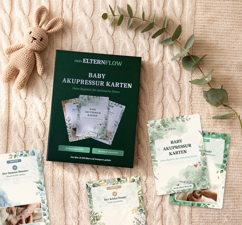 K&ouml;nnte beinhalten: Eine dunkelgr&uuml;ne Schachtel mit der Aufschrift DEIN ELTERNFLOW BABY AKUPRESSUR KARTEN, dazu mehrere Anleitungskarten mit gr&uuml;nen botanischen Illustrationen, ein kleines geh&auml;keltes beiges H&auml;schen und ein gr&uuml;ner Blattzweig auf strukturiertem cremefarbenem Stoff.