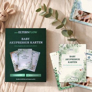 K&ouml;nnte beinhalten: Eine dunkelgr&uuml;ne rechteckige Schachtel mit der Aufschrift DEIN ELTERNFLOW BABY AKUPRESSUR KARTEN sowie mehrere Lernkarten mit botanischen Aquarellillustrationen, Text und Diagrammen zu Baby-Akupressurtechniken auf beigem Strickstoff.
