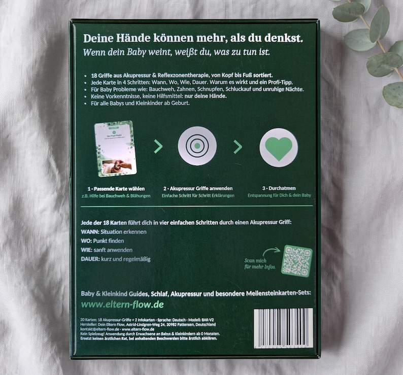 K&ouml;nnte beinhalten: Eine dunkelgr&uuml;ne rechteckige Schachtel mit deutschem Text und grafischen Anleitungen zur Baby-Akupressur. Die R&uuml;ckseite zeigt einen dreistufigen Prozess mit Symbolen, einem QR-Code, einem Barcode und Informationen zu 18 Akupressur-Karten.