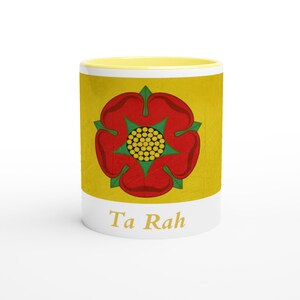 May include: A white ceramic mug with a yellow interior and exterior. The mug features a red rose design with green leaves and a yellow center. The words "Ta Rah" are printed in a white band at the bottom of the mug.