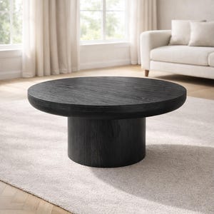 May include: A round, black coffee table with a thick, solid base. The table has a dark wood grain finish and sits on a light-colored rug. The table's design is modern and minimalist, suitable for a living room setting.