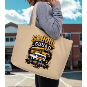 May include: A beige canvas tote bag featuring a graphic print of a yellow school bus and a white van. The text reads SCHOOL SQUAD and WE ROLL TOGETHER. The design includes decorative flourishes and a star icon, centered on the front of the bag.