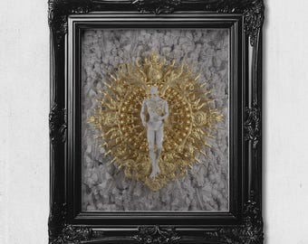 May include: A framed artwork featuring a central white human figure standing within a gold, ornate, sunburst-style circular frame. The background consists of a dense, textured pattern of small white skeletal figures, all enclosed in a black frame.