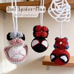 Puede incluir: Tres adornos colgantes de ganchillo con personajes de Spider-Man, incluyendo una versión blanca y rosa, una negra y roja, y una roja y azul, con una telaraña de ganchillo blanca y el texto 3in1 Spider-Man PDF pattern.