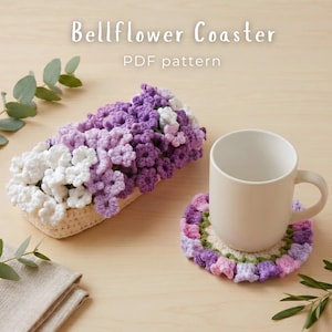 Può includere: Un sottobicchiere all'uncinetto a forma di campanule e un contenitore rettangolare all'uncinetto riempito di fiori bianchi e viola. Il testo Bellflower Coaster PDF pattern è visibile. Una tazza in ceramica bianca poggia sul sottobicchiere.