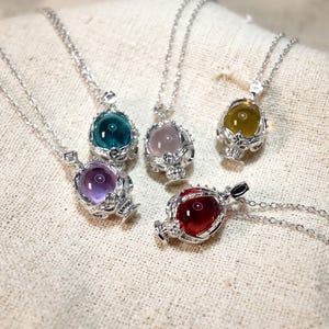 Puede incluir: Una colección de cinco collares con colgantes de piedras preciosas. Cada collar presenta una piedra preciosa de diferente color: morado, turquesa, rosa, amarillo y rojo. Las piedras están engastadas en filigranas plateadas ornamentadas.