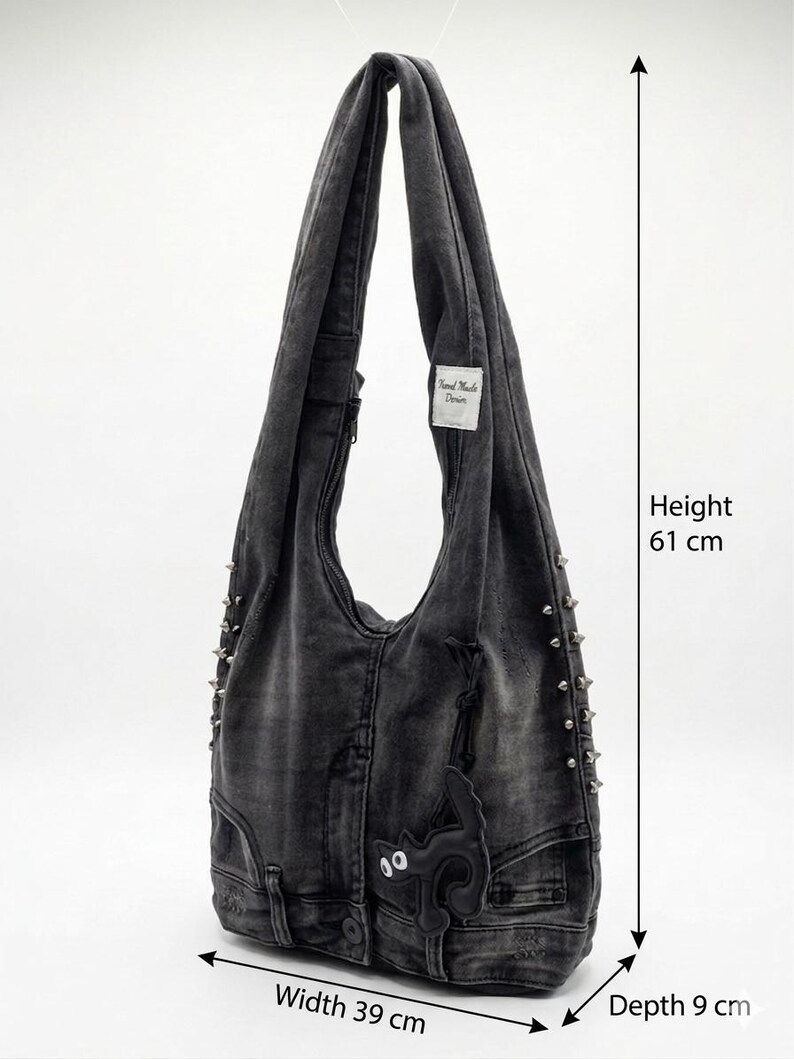 May include: A gray denim shoulder bag with a black cat applique and silver studs. The bag is 24 inches tall, 15 inches wide, and 3.5 inches deep. Features a label that reads "Hand Made Denim".