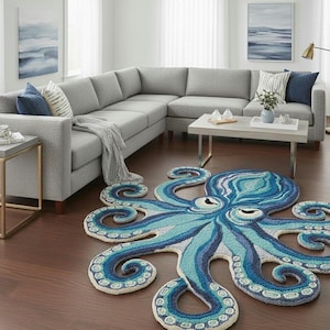 May include: A blue and white octopus rug in a living room setting. The rug is placed on a wooden floor, with a grey corner sofa and a coffee table. The octopus design features intricate details and varying shades of blue.