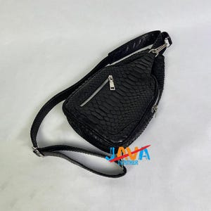 Peut inclure: Sac bandoulière noir avec un motif en peau de serpent texturé. Le sac comporte un compartiment principal zippé et une petite poche avant, tous deux avec des fermetures éclair argentées. La bandoulière réglable est également noire et texturée.