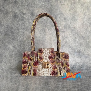Peut inclure: Sac à main rectangulaire avec un motif peau de serpent dans les tons bordeaux, jaune et crème. Le sac est doté d'une poignée incurvée et d'un fermoir doré. Le sac mesure environ 25 cm de large et 18 cm de haut.