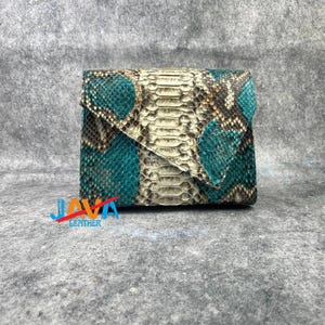 Peut inclure: Un portefeuille carré et plié en peau de serpent. Le portefeuille présente un motif turquoise, marron et crème. Le rabat est turquoise et le corps du portefeuille présente un mélange de couleurs. Le portefeuille est de petite taille.