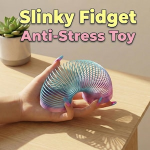 May include: A rainbow-colored Slinky Fidget Anti-Stress Toy is held in a hand. The toy is made of metal and has a spiral design. The text "Slinky Fidget Anti-Stress Toy" is displayed in yellow and pink.