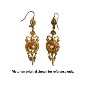Peut inclure: Une paire de boucles d'oreilles pendantes dor&eacute;es. Chaque boucle d'oreille pr&eacute;sente un motif floral avec une perle centrale, des &eacute;l&eacute;ments d&eacute;coratifs et trois pendentifs coniques. Le texte "Victorian original shown for reference only" est en bas.