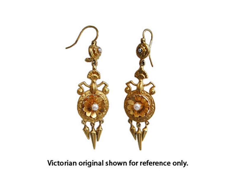 Peut inclure: Une paire de boucles d'oreilles pendantes dor&eacute;es. Chaque boucle d'oreille pr&eacute;sente un motif floral avec une perle centrale, des &eacute;l&eacute;ments d&eacute;coratifs et trois pendentifs coniques. Le texte "Victorian original shown for reference only" est en bas.