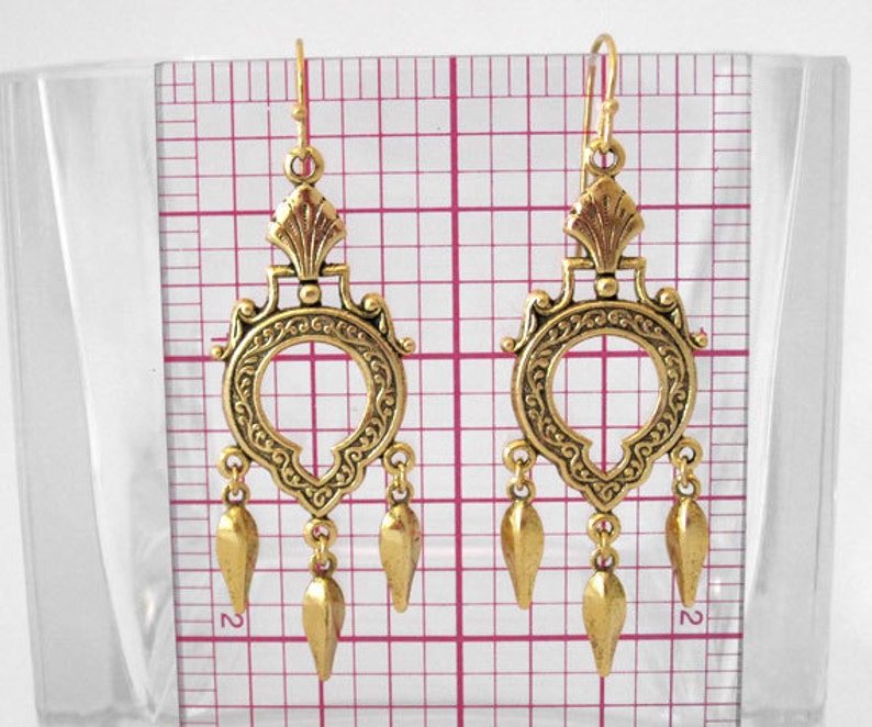 Peut inclure: Une paire de boucles d'oreilles pendantes dor&eacute;es et orn&eacute;es. Chaque boucle d'oreille pr&eacute;sente un dessus d&eacute;coratif avec un motif circulaire et trois pendentifs en forme de goutte. Les boucles d'oreilles mesurent environ 7.6 cm de long.