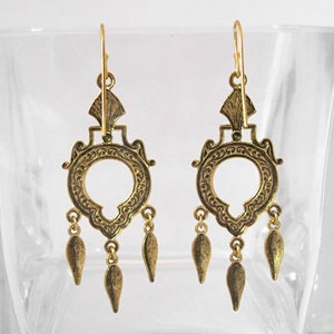 Peut inclure: Une paire de boucles d'oreilles dor&eacute;es de style chandelier. Chaque boucle d'oreille pr&eacute;sente un motif circulaire avec des d&eacute;tails orn&eacute;s, un dessus d&eacute;coratif et trois pendentifs en forme de goutte. Les boucles d'oreilles sont pr&eacute;sent&eacute;es sur un fond clair.