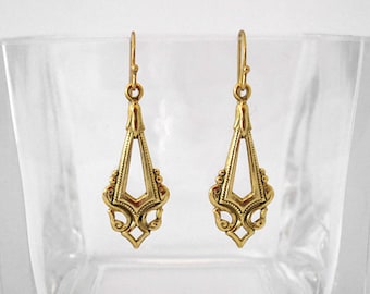 May include: A pair of gold-colored, Art Deco-style earrings. Each earring features a long, openwork design with a central geometric shape and ornate detailing. The earrings have a hook closure.