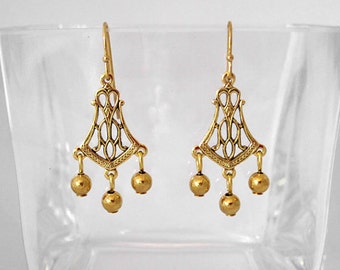 May include: Gold dangle earrings with a geometric design and three round beads hanging from each earring.