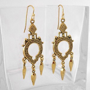 Peut inclure: Une paire de boucles d'oreilles pendantes dor&eacute;es. Chaque boucle d'oreille pr&eacute;sente un motif orn&eacute; avec un centre circulaire, des filigranes d&eacute;coratifs et trois pampilles en forme de goutte. Les boucles d'oreilles ont une fermeture &agrave; crochet.