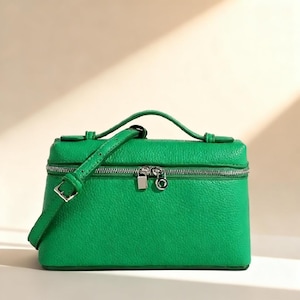 May include: A bright green, rectangular handbag with a top handle and a detachable shoulder strap. The bag features a silver zipper closure and hardware. The leather-like material has a textured appearance. The bag is designed to be carried by hand or over the shoulder.