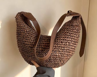 May include: A woven brown shoulder bag with a curved shape. The bag features a brown leather strap and a matching leather accent at the top. The bag is made of a tightly woven material, giving it a textured appearance.