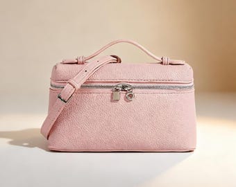 May include: A light pink, textured cosmetic bag with a silver zipper and hardware. The bag has a top handle and a detachable shoulder strap. The bag is rectangular with rounded corners.