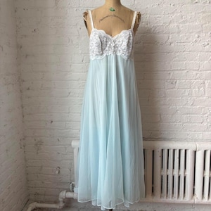 May include: A vintage light blue nightgown with a white lace bodice and spaghetti straps. The long, flowing gown is displayed on a mannequin against a white brick wall. The nightgown is made of a sheer, lightweight fabric.