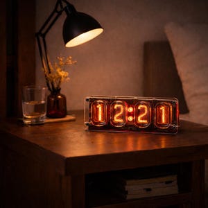 Puede incluir: Un reloj digital de estilo retro que muestra "12:21" en números naranjas brillantes. El reloj está encerrado en un marco rectangular transparente y se encuentra sobre una mesita de noche de madera oscura. También hay una lámpara de escritorio negra y un vaso de agua.