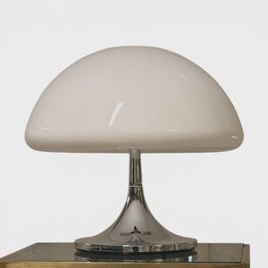May include: A white, dome-shaped table lamp with a chrome base and stem. The lamp sits on a small, square table with a gold-colored frame. The lamp's shade is a smooth, opaque white.