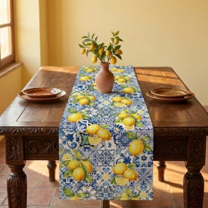 May include: A blue and white patterned table runner with a lemon design, placed on a dark wooden table. A small brown vase holds a lemon branch. Two brown plates are on the table.