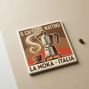 Op de afbeelding: Vierkante keramische tegel met een vintage illustratie van een espressopot, een koffiekopje en stoom in de vorm van een hart. De tegel heeft de tekst "IL CAFFÈ DEL MATTINO" en "LA MOKA - ITALIA". Een koffieboon ligt ernaast.
