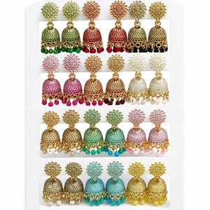 Könnte beinhalten: Eine Präsentation von farbenfrohen, verzierten Jhumka-Ohrringen. Jeder Ohrring hat eine florale Oberseite und einen glockenförmigen Boden, verziert mit Perlen. Farben sind Grün, Rot, Rosa, Gold, Blau und Gelb. Die Ohrringe sind auf einem weißen Display angeordnet.