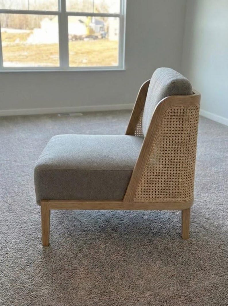 May include: A modern accent chair with a gray upholstered seat and back. The chair features a natural wood frame with woven cane detailing on the back. The chair is set on four wooden legs and is designed for comfort and style.