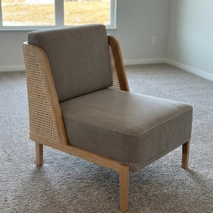 May include: A modern accent chair with a light gray upholstered seat and back. The chair features natural wood framing and woven cane side panels. The chair has four wooden legs and is designed for comfort and style.