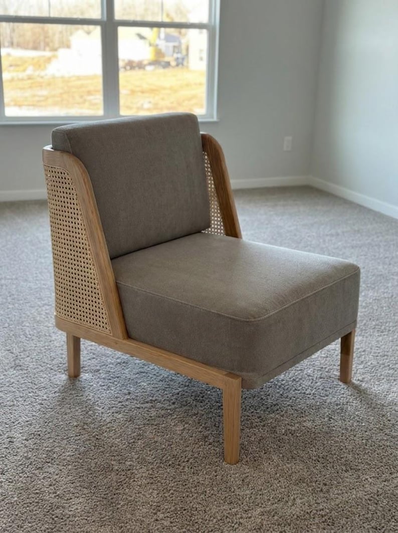 May include: A modern accent chair with a light gray upholstered seat and back. The chair features natural wood framing and woven cane side panels. The chair has four wooden legs and is designed for comfort and style.