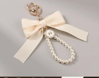 Sleutelhanger met parelstrik: crèmekleurige tasbedel met bloemenhanger