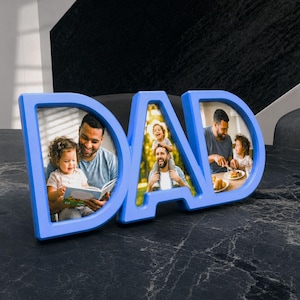 May include: A light blue photo frame in the shape of the word "DAD". The frame holds three family photos. The photos show a father and child reading a book, a father carrying a child on his shoulders, and a father and child eating.