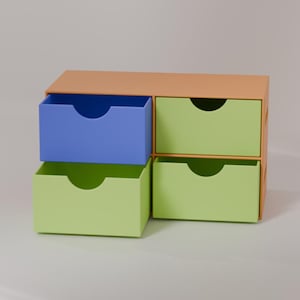 May include: A small, colorful storage unit with four drawers. The top is a light orange, with two green drawers and one blue drawer visible. The fourth drawer is also green. Each drawer has a curved handle cutout.