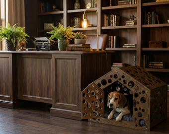 Puede incluir: Una caseta para perros de madera con recortes circulares se encuentra junto a un gran escritorio de madera. Un beagle está dentro de la caseta. El escritorio tiene una máquina de escribir, plantas y una lámpara. Estanterías llenas de libros están en el fondo.