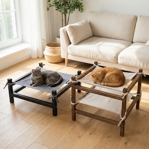 May include: Two cat beds with cats resting on them. One bed is black with a gray fabric, the other is brown with a white fabric. The beds are made of wood and have a hammock-like design. The cats are gray and orange.