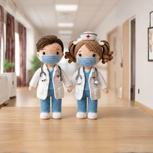 May include: Two crocheted dolls depicting medical staff, a doctor and a nurse, holding hands. They wear blue scrubs, white coats, and face masks. Each doll has a stethoscope and a cross emblem. The nurse doll wears a white cap with a red cross.