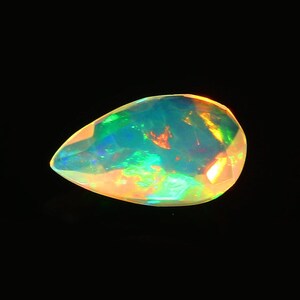 May include: A pear-shaped opal gemstone with a vibrant display of colors, including green, blue, orange, and yellow. The gemstone is set against a black background, highlighting its iridescent qualities.