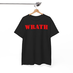 May include: Black t-shirt with the word "WRATH" printed in bold red letters across the chest. The shirt is hanging on a wooden hanger, suspended from a metal bar. The design is simple and eye-catching.