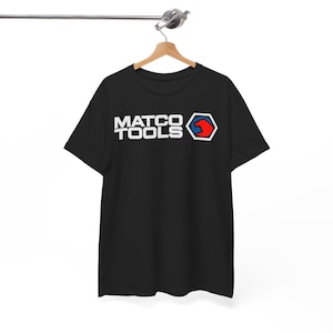 Può includere: T-shirt nero con la scritta bianca "MATCO TOOLS" e un logo rosso e blu. La t-shirt è appesa a una gruccia di legno.