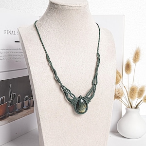 Puede incluir: Un collar de macramé verde oscuro con un colgante de piedra preciosa verde en forma de lágrima.