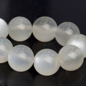 Könnte beinhalten: Eine Kette aus weißen Mondsteinperlen. Die Perlen sind rund und glatt, mit einem subtilen Schimmer.