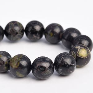 May include: A strand of black and green gemstone beads. The beads are round and have a speckled pattern.
